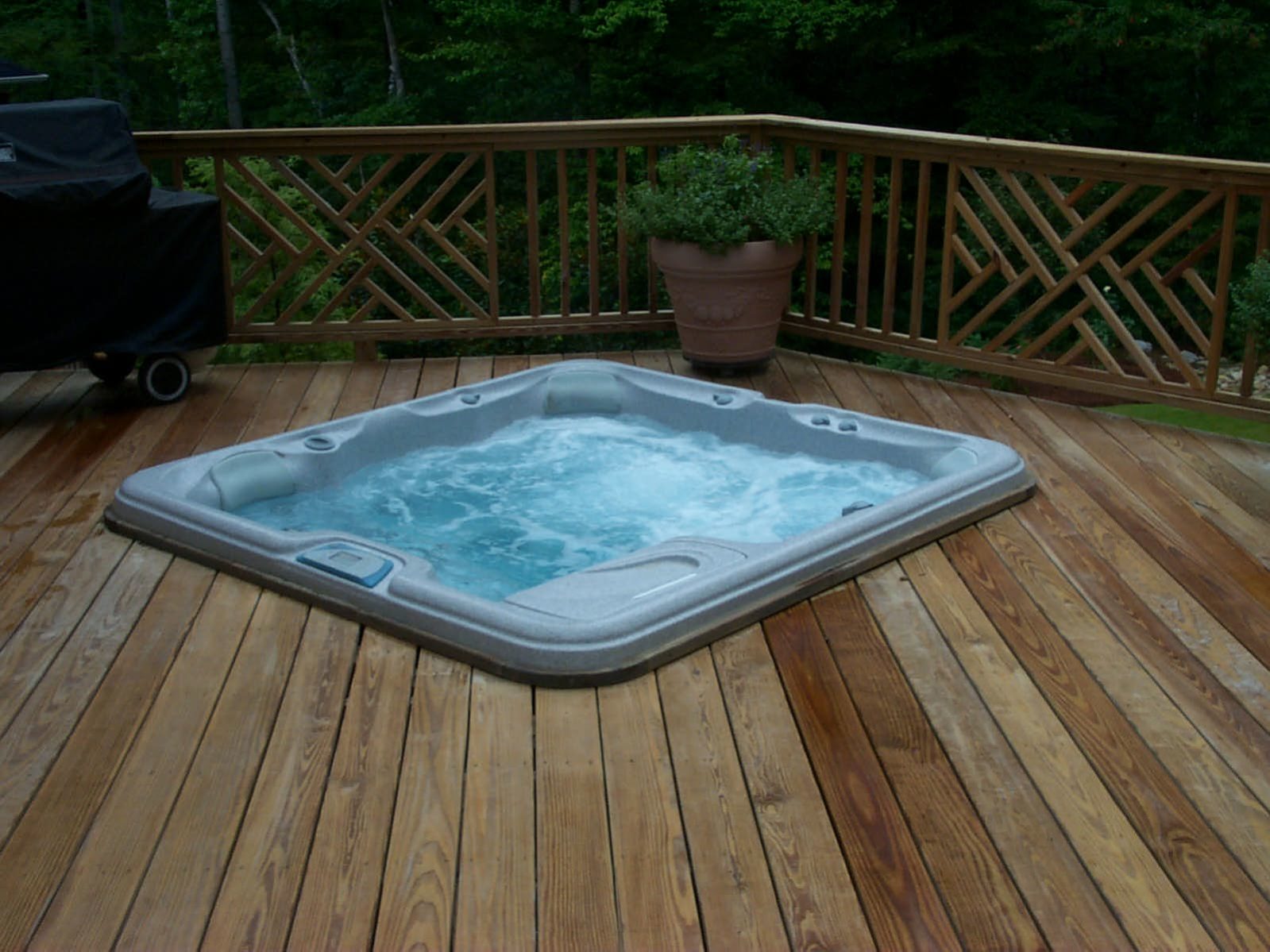 A rustic deck cradles the hot tub, surrounded by lush greenery and potted plants, creating a tranquil oasis.