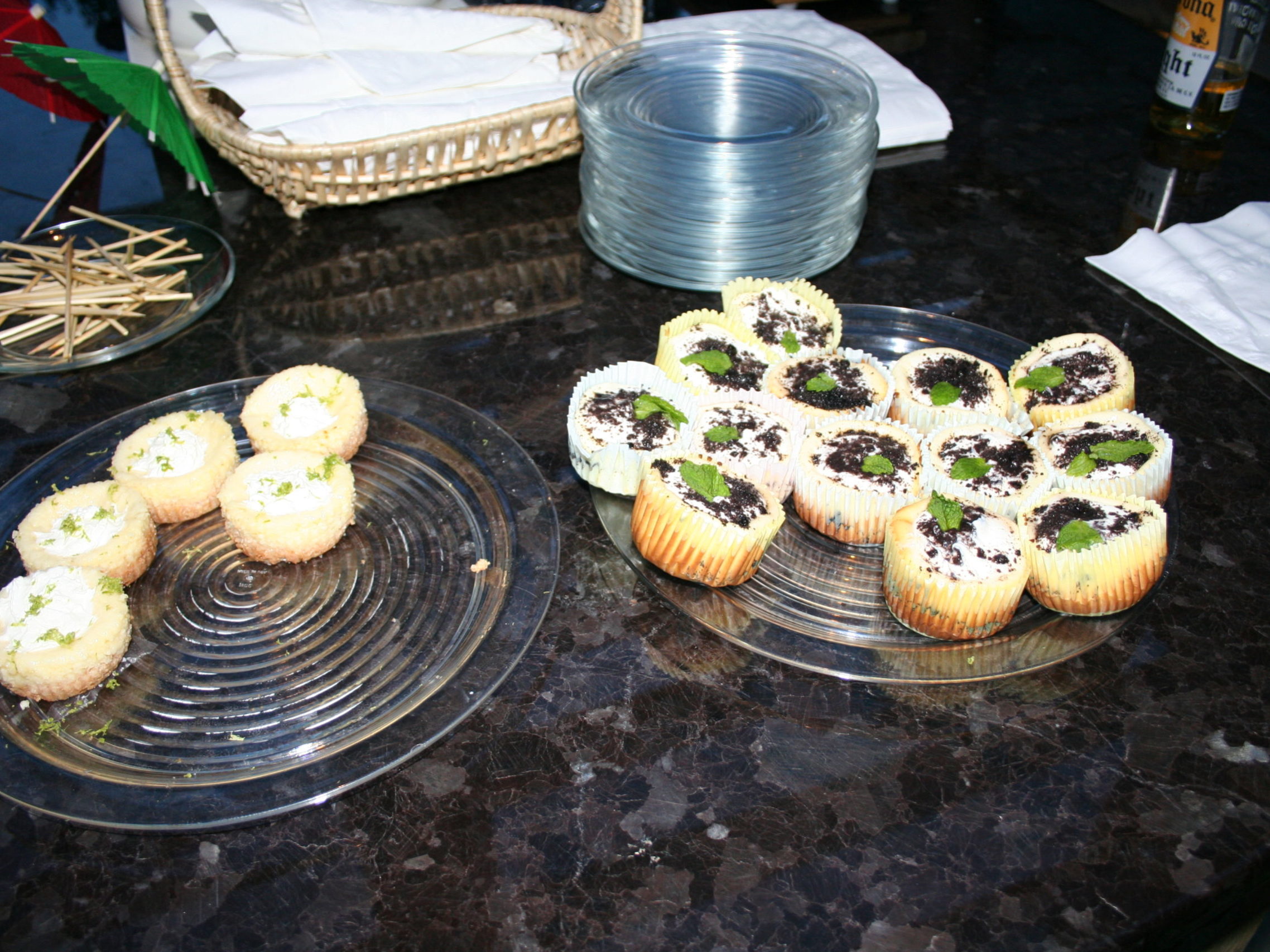 Two plates of cupcakes on a dark countertop: left plate with six plain cupcakes, right plate with cupcakes topped with crumbled cookies and mint leaves, perfect treats for an outdoor kitchen gathering by the fireplace.