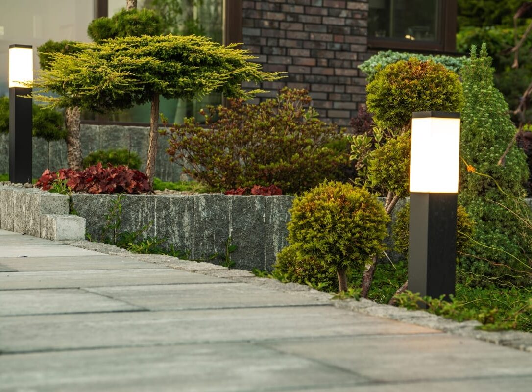 The illuminated pathway boasts energy-efficient landscape lighting with modern rectangular fixtures, bordered by neatly trimmed shrubs and small trees on a stone-paved path. The illuminated pathway boasts energy-efficient landscape lighting with modern rectangular fixtures, bordered by neatly trimmed shrubs and small trees on a stone-paved path.