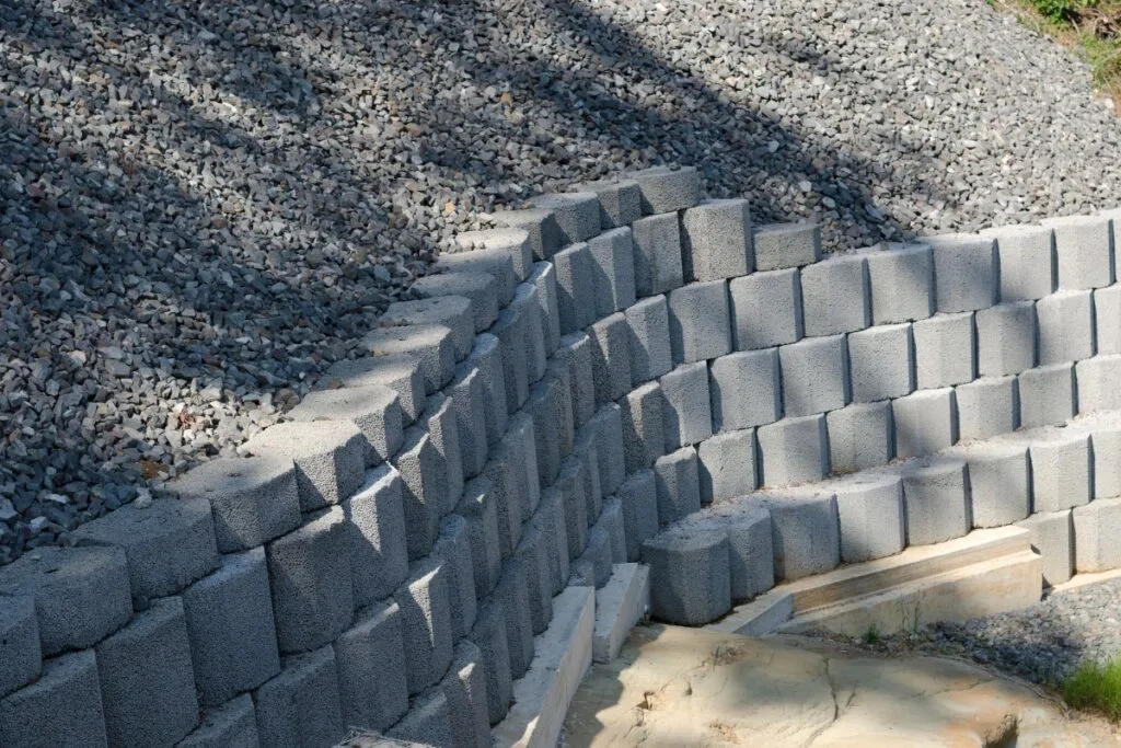 Learn how to build a retaining wall with interlocking concrete blocks, perfectly set against a sloped pile of loose gravel.