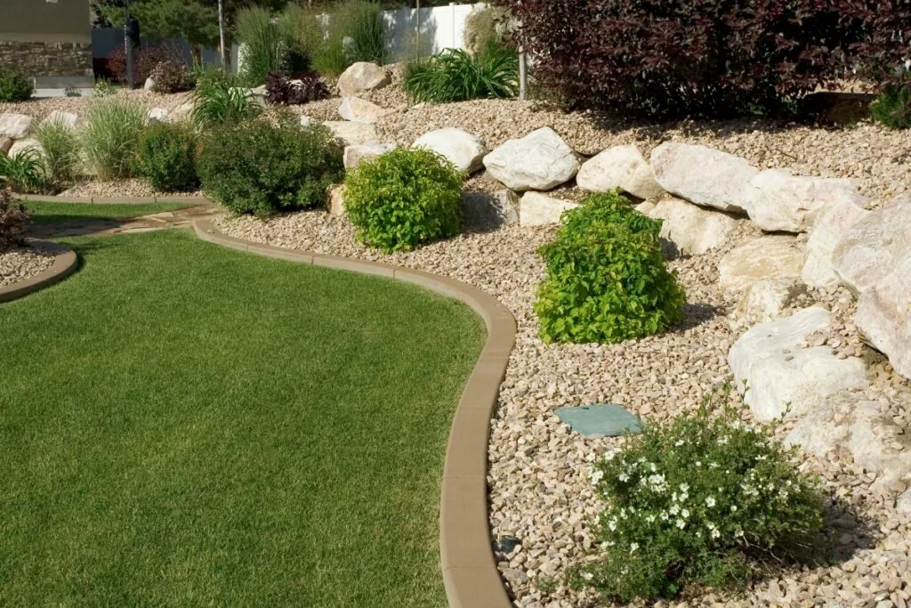 A beautifully landscaped garden in Georgia features a curved grass pathway, bordered by rocks, plants, and gravel mulch. This example of sustainable landscaping showcases the area's natural beauty while promoting eco-friendly practices.