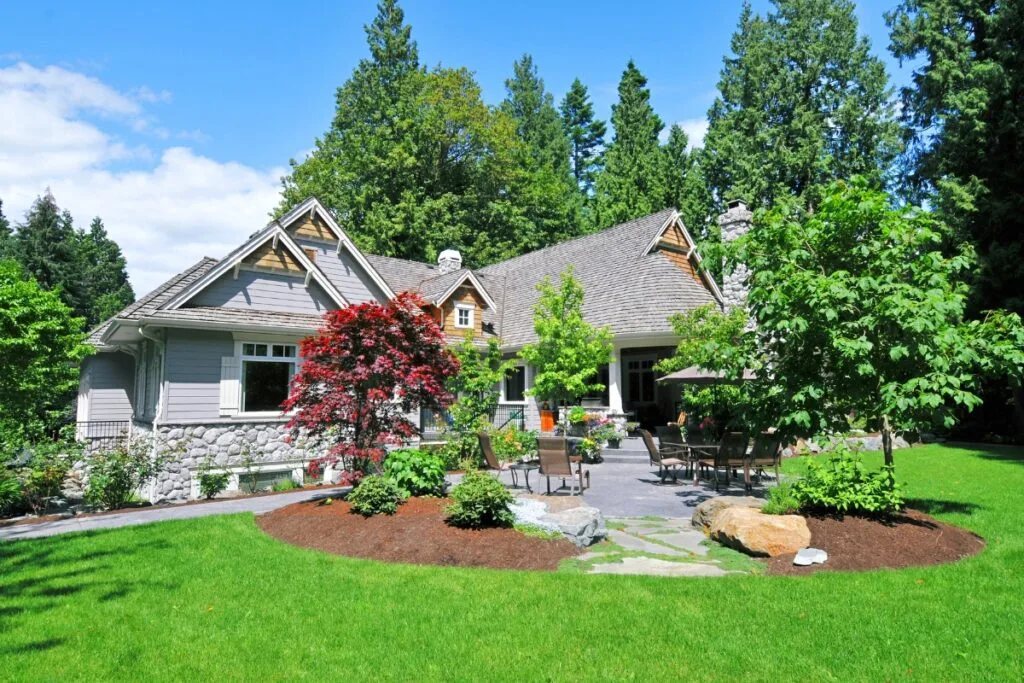 Gray single-story house with stone accents, featuring sustainable landscaping in Georgia. It's surrounded by lush greenery and a landscaped yard with patio furniture, all basking in the sun's warm embrace.