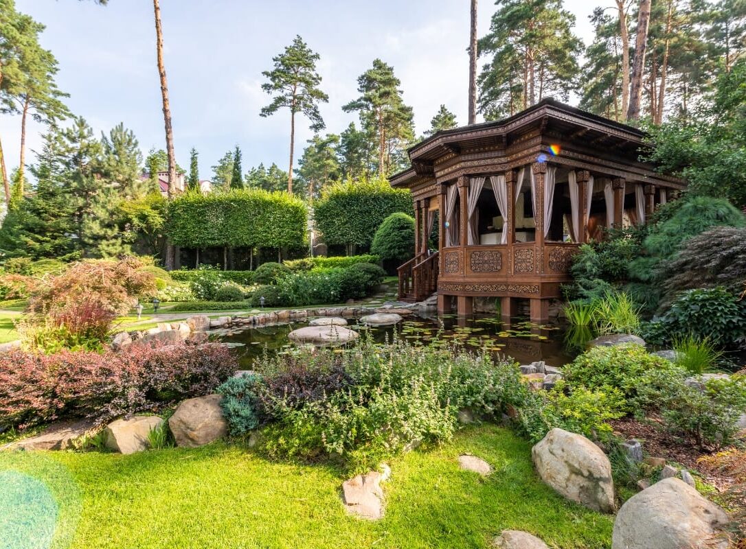 A wooden gazebo by a pond is nestled amidst lush greenery and rocks in this expertly crafted landscape design in Cherokee County. Tall trees form the backdrop under a clear sky, creating an enchanting garden retreat. A wooden gazebo by a pond is nestled amidst lush greenery and rocks in this expertly crafted landscape design in Cherokee County. Tall trees form the backdrop under a clear sky, creating an enchanting garden retreat.