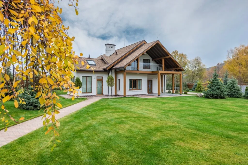 A modern house with a sloped roof and large windows, expertly nestled in Cherokee County's stunning landscape design, surrounded by a neatly manicured lawn and trees showcasing vibrant autumn foliage.