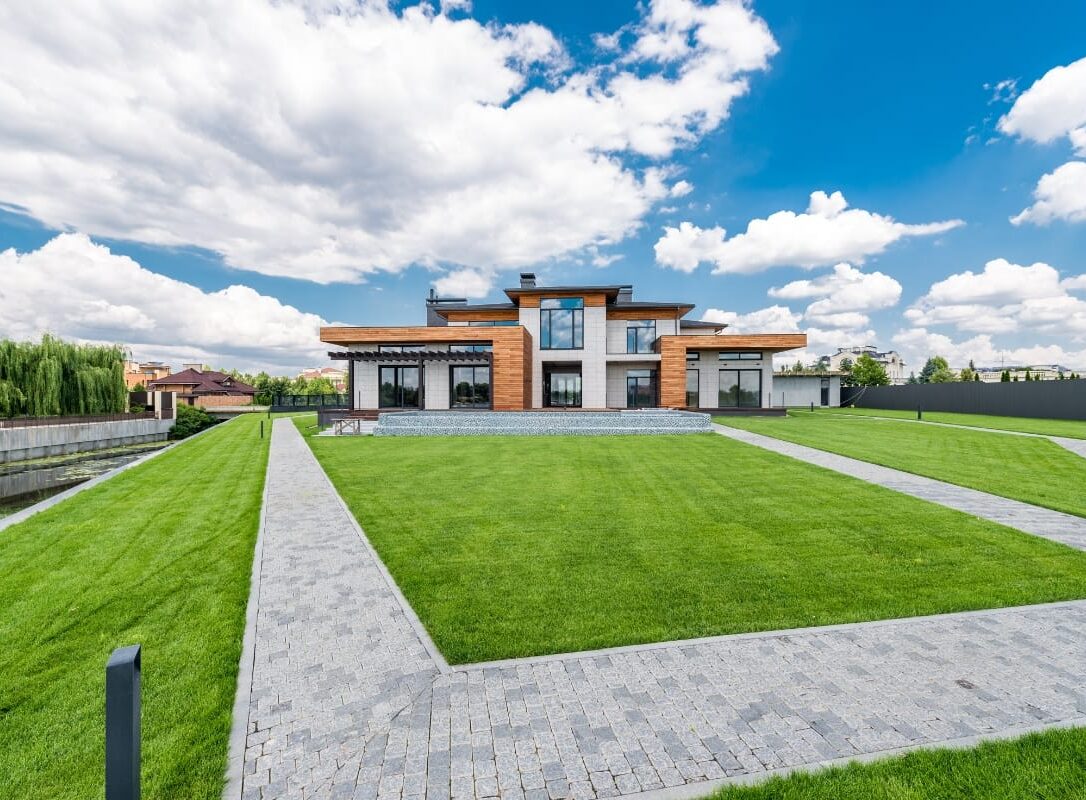 Modern two-story house with large windows and wood accents, surrounded by a luxury landscape design in Georgia, featuring a well-kept lawn and paved walkways under a partly cloudy sky. Modern two-story house with large windows and wood accents, surrounded by a luxury landscape design in Georgia, featuring a well-kept lawn and paved walkways under a partly cloudy sky.