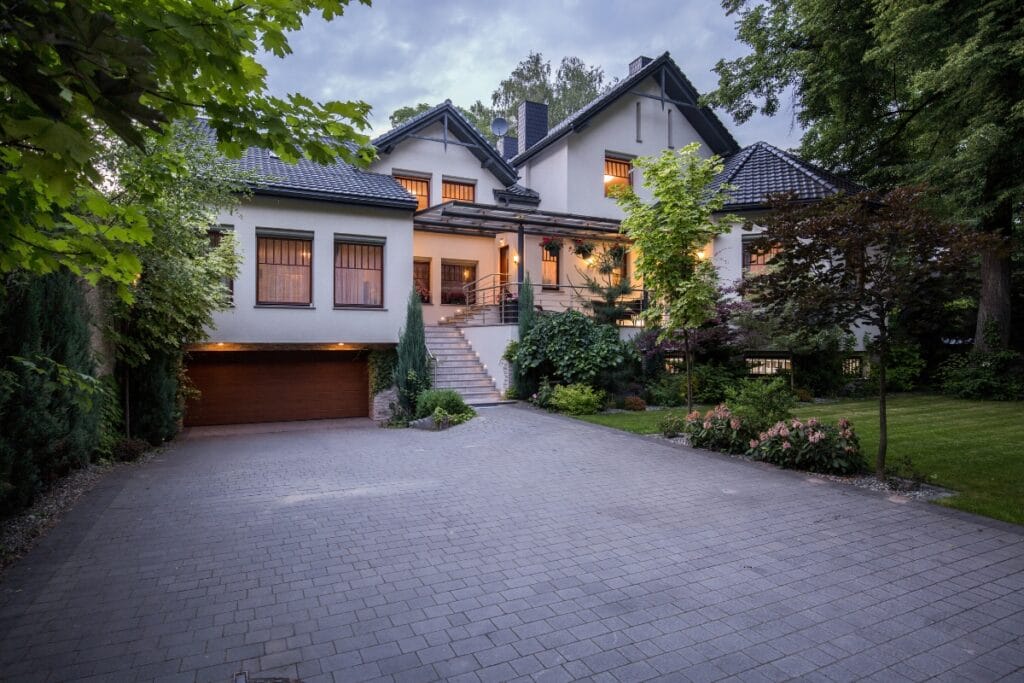Large two-story house with a pitched roof, illuminated windows, double garage, front steps, and surrounded by trees and Luxury Landscape Design in Georgia-inspired greenery at dusk.