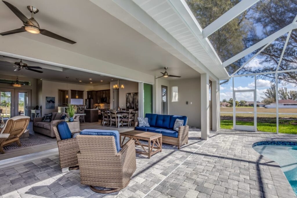 Spacious patio with wicker furniture and blue cushions, connected to an open indoor living area, overlooks the pool and screened outdoor space—your perfect Cobb County backyard retreat.