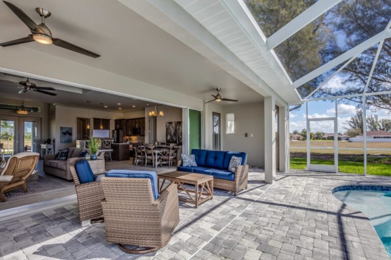 Spacious patio with wicker furniture and blue cushions, connected to an open indoor living area, overlooks the pool and screened outdoor space—your perfect Cobb County backyard retreat.