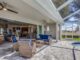 Covered patio with blue cushioned wicker furniture creates an inviting outdoor living space that flows into a modern living room and kitchen; screened enclosure overlooks a backyard and pool.