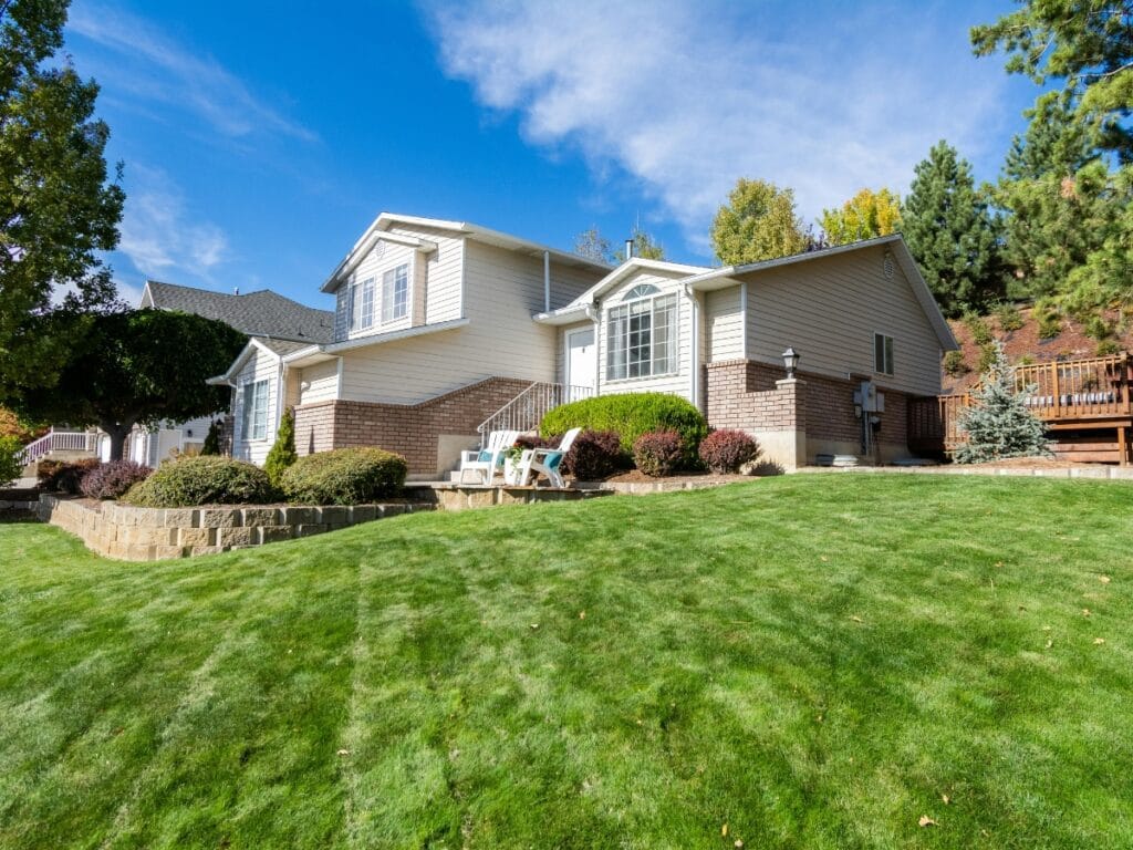 Single-story house with brick and siding exterior, surrounded by expert landscape design featuring a well-maintained lawn, shrubs, and trees under a clear blue sky.