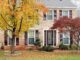 Two-story brick house with maroon shutters and front door, beautifully landscaped yard featuring trees in peak autumn foliage—perfect inspiration for your own home’s curb appeal and fall landscaping tips.