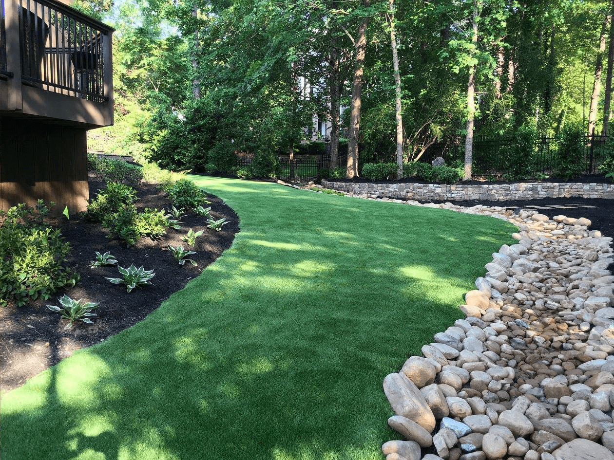 Low-maintenance backyard featuring artificial turf, a dry creek bed, and smooth white stones. See similar projects on our blog.