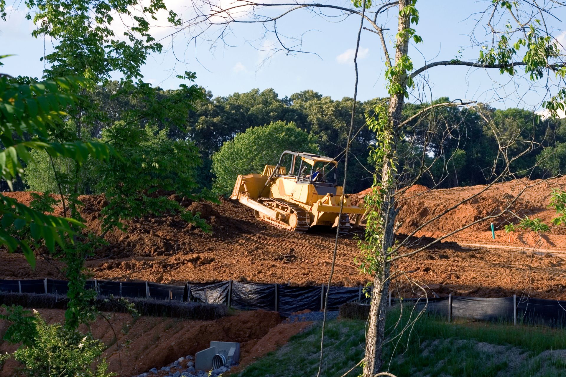 Bulldozer leveling soil on a construction site in Atlanta, surrounded by greenery and erosion control barriers, highlighting grading services for outdoor projects.