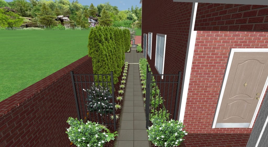 Narrow paved walkway beside a red brick house, bordered by metal fencing, green shrubs, and small plants, with a grassy lawn and trees in the background&mdash;ideal for placing a dynamic content widget for vibrant outdoor updates.