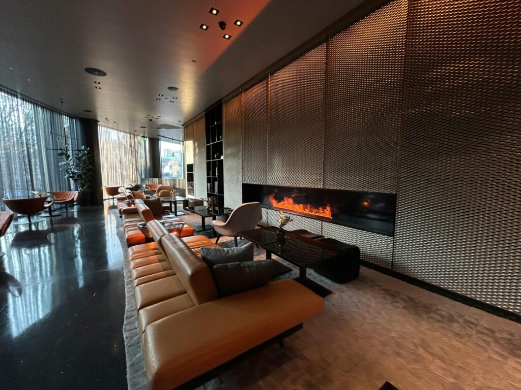Modern lounge area with tan leather seating, a long linear fireplace, floor-to-ceiling windows, and contemporary decor—perfect for relaxing by one of the most stylish fireplaces in the city.