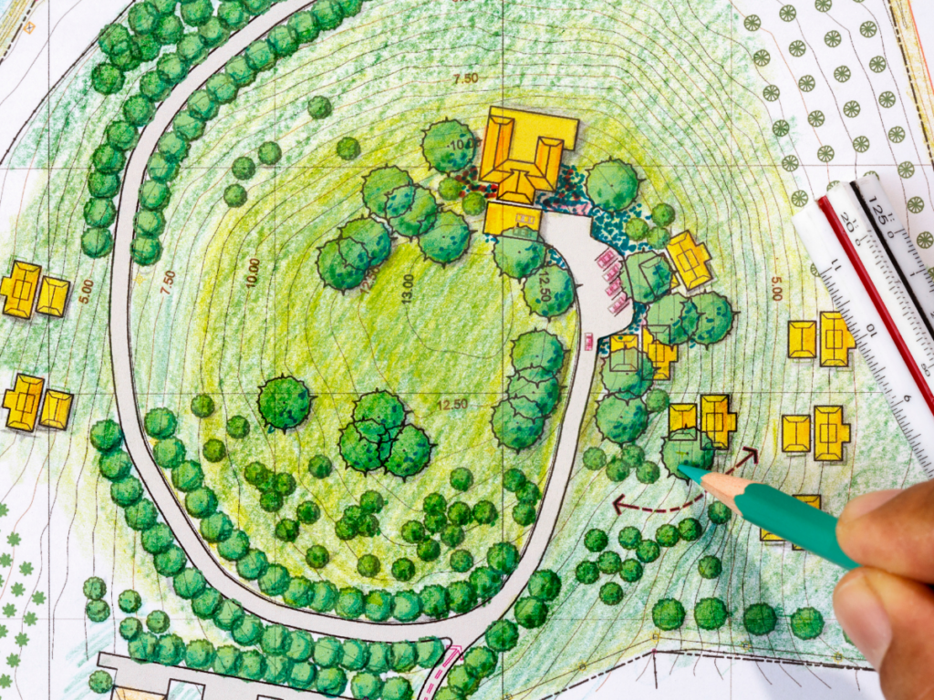A hand drawing on a landscape site plan with trees, buildings, paths, and elevation contours, using a green pencil and a scale ruler, highlighting design elements that can offer health benefits to the community.