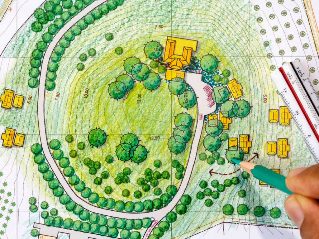 Hand drawing on a colored landscape architectural site plan with trees, paths, buildings, and a scale ruler visible, illustrating concepts that can be further enhanced through 3D landscape designs.