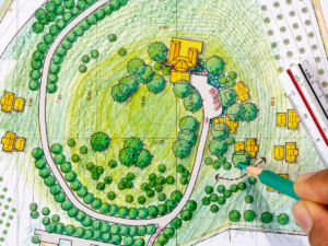 Hand drawing on a colored landscape architectural site plan with trees, paths, buildings, and a scale ruler visible, illustrating concepts that can be further enhanced through 3D landscape designs.